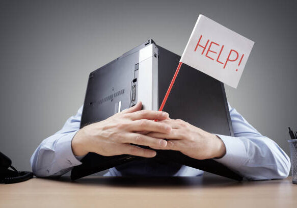 24-124 Frustrated and overworked businessman burying his head uner a laptop computer asking for help
